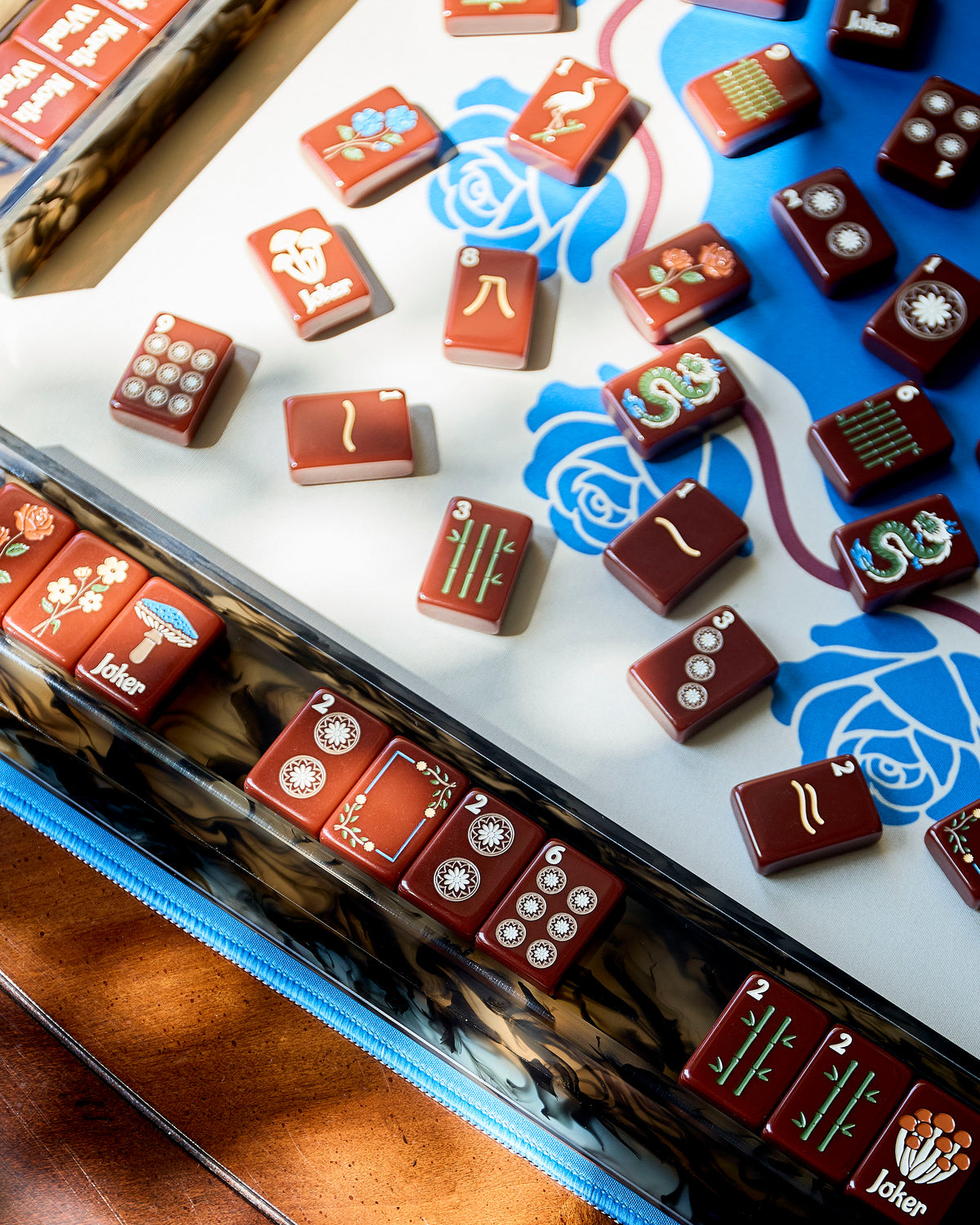 The Redemption Line mahjong tiles and an acrylic mahjong rack on a blue rose mahjong mat